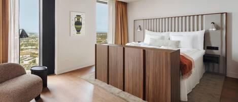 Habitación de hotel moderna con una cama grande, un armario de madera, zona de estar y vistas a la ciudad.