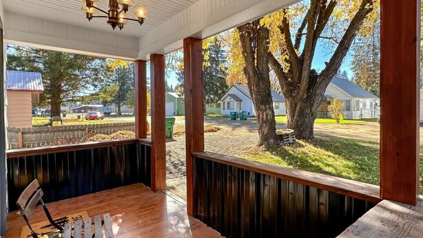 A covered outdoor seating area with wooden benches and a table, overlooking a residential neighborhood with houses and trees. - Charming Cascade Cabin: Large Yard, Near Downtown! (Cascade)
