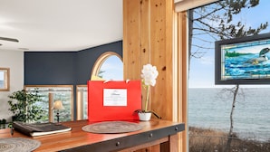 Un bureau en bois sur lequel se trouvent un classeur rouge, une plante en pot et un cadre représentant un paysage lacustre.