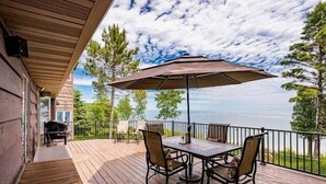 Une terrasse en bois avec une table et des chaises, un parasol et une vue sur l’océan.