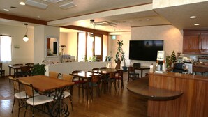Un amplio comedor con mesas y sillas de madera, una barra y un televisor de pantalla plana grande montado en la pared.