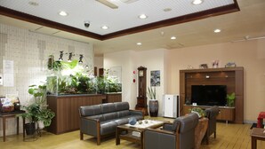 Un salón amplio con un sofá, sillones, una mesa de centro y un televisor. Se observan plantas en macetas y un aparador de madera.
