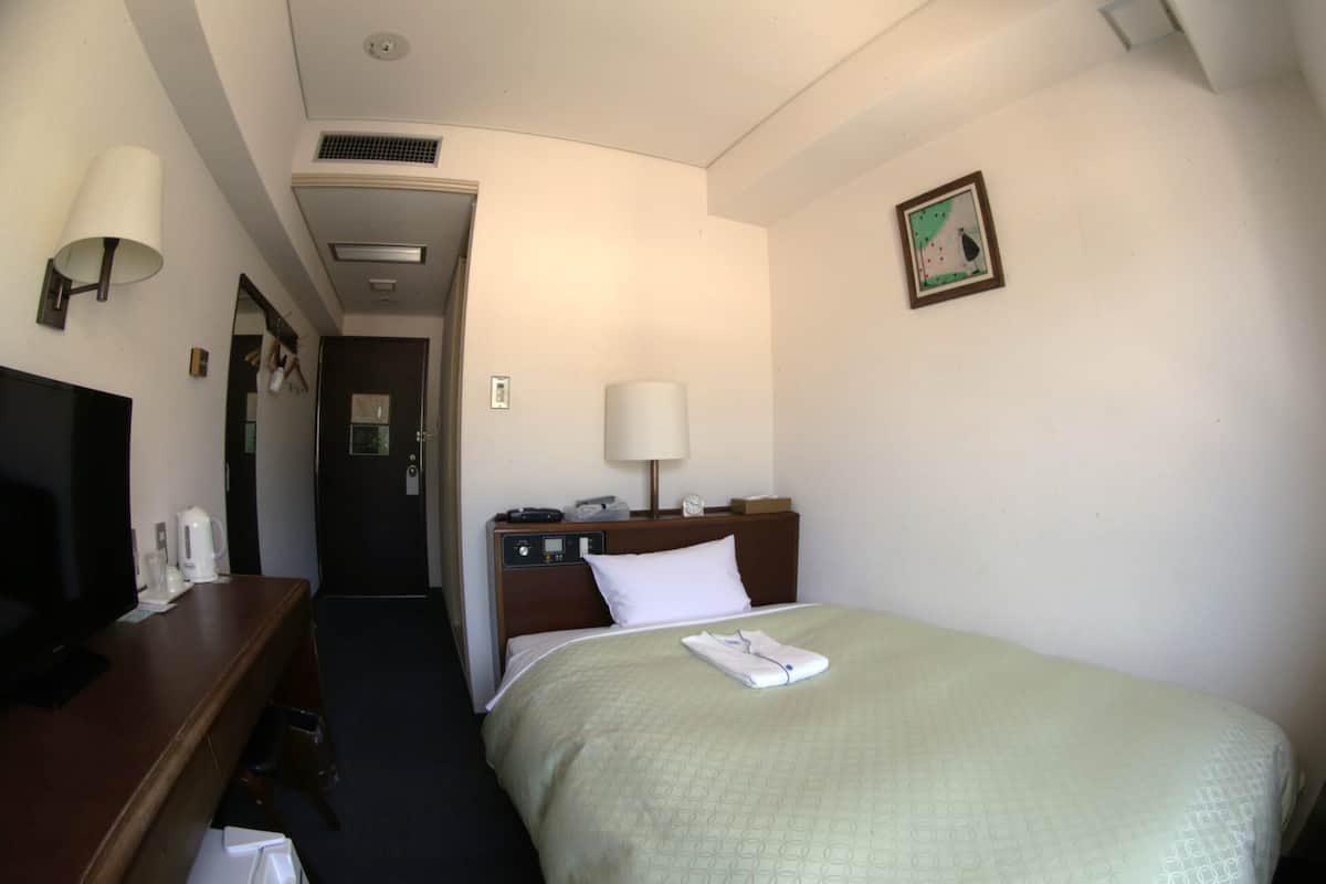 A hotel room with a bed, a desk with a lamp, a television, and a painting on the wall.