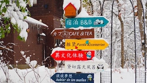 A signpost with multiple directional signs pointing to various establishments, including a cafe, tea shop, and panda accessories store. - Pension Snowfall Meteor (Kaminoyama)