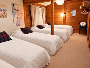 Habitación con tres camas, paredes de madera, una lámpara colgante y una pequeña mesa con una silla.