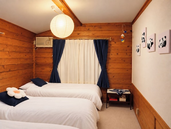 Una habitación con dos camas, techo de madera, lámpara colgante, ventana con cortinas y decoración en la pared.