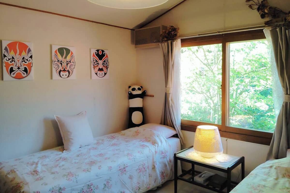 A room with a bed, a bedside table with a lamp, and three wall-mounted paintings.