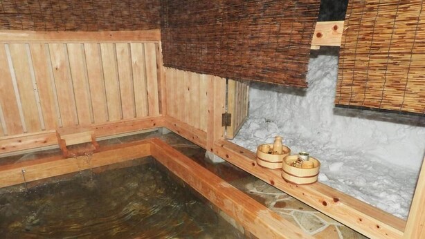A wooden sauna with a stone floor, wooden benches, and a stone wall. - Pension Snowfall Meteor (Kaminoyama)