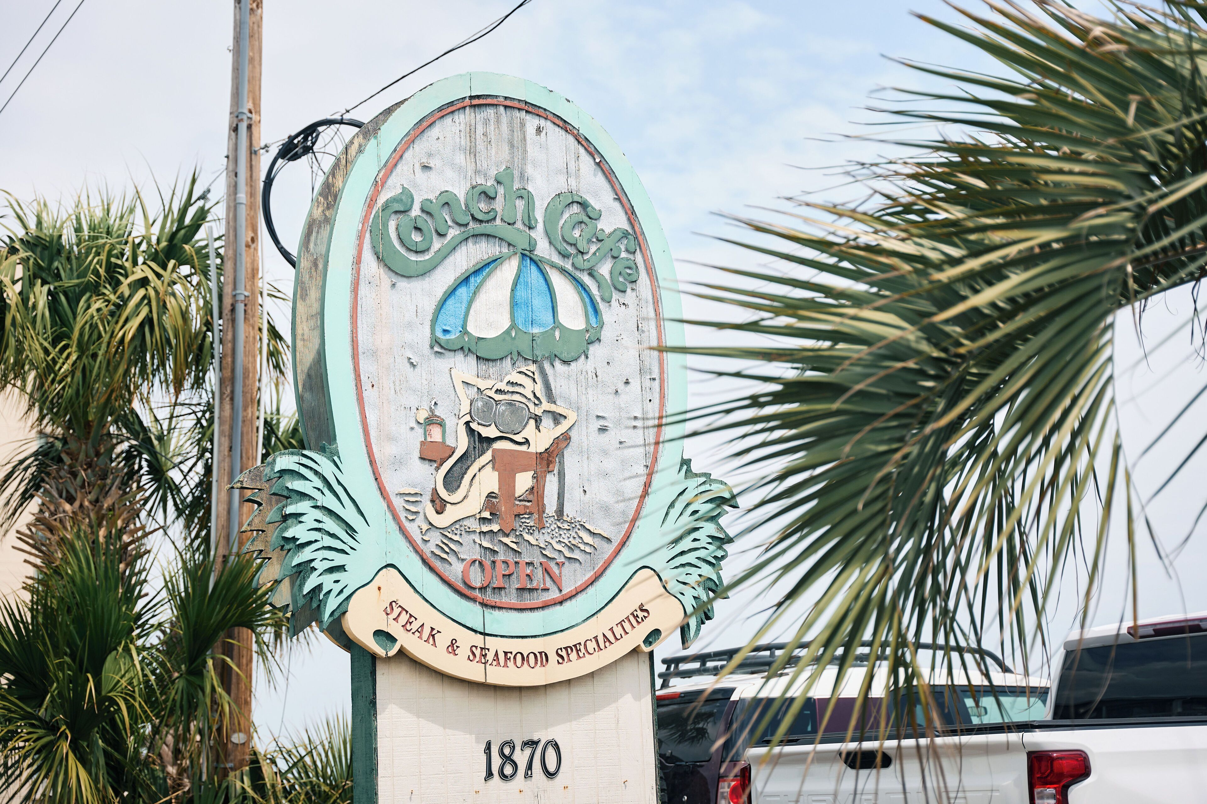 Señal antigua de un restaurante llamado 'Conch Cafe' con la fecha '1870' y un logotipo que muestra una caracola y un pez.