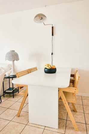 A white dining table with a bowl of fruit, a lamp, and chairs. - Top Floor Surfside Beach Condo with Pool & Easy Beach Access, Pets Welcome  (Surfside Beach)