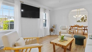 Un soggiorno moderno con TV a schermo piatto, arredi in legno, un'area pranzo e vista sul verde.
