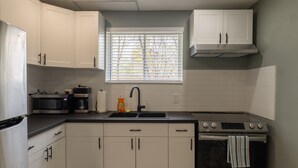 A kitchen with white cabinets, a black countertop, a microwave, a coffee maker, a sink, and a stove.
