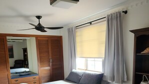 Una camera da letto con un letto, una ventola a soffitto, una finestra con tende, un armadio e un comodino.