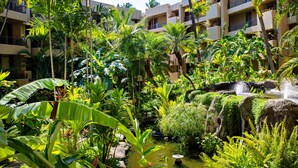 Ein üppiger Innenbereichsgarten mit Wasserspiel, umgeben von mehrstöckigen Gebäuden mit Balkonen.