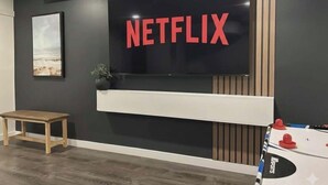 A modern living room with a large flat-screen TV mounted on a dark wall, a wooden bench, and a foosball table. - Lovelyhome•Near BU•With TreeHouse•Ideal for group stays (Brandon)