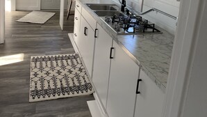 Cozinha moderna com armários brancos, pia de aço inoxidável e bancada de mármore.