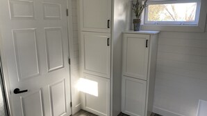 Um canto de quarto com armários brancos, uma janela com vista para árvores e uma porta.