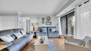 Ein Wohnzimmer mit grauem Sofa, weißem Couchtisch und blauem Sofa. An den Wänden befinden sich Dekorationen, darunter ein Walgemälde und ein Holzschild.