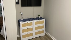 Ein Zimmer mit einer weißen Kommode, einem kleinen Topfpflanzen und einem flach an der Wand befestigten Flachbildfernseher.