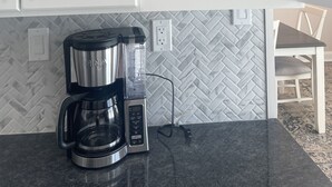 A kitchen with white cabinets, a coffee maker, and a herringbone-patterned backsplash.