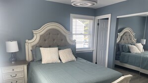 A bedroom with a bed, nightstand, dresser, and a window with blinds.