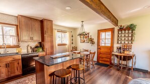 A spacious kitchen with wooden cabinets, a large island with stools, a dining area with a table and chairs, and a built-in shelf with kitchenware. - The Bartlett Nook/ HOT TUB/ 3-BEDROOM/ 4 BEDS/ CLOSE TO LU (Lynchburg)