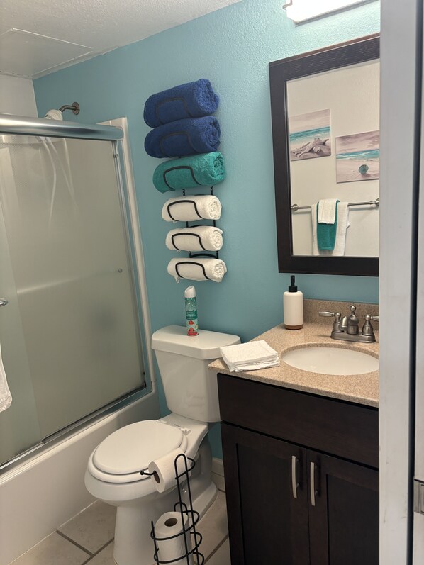A bathroom with a shower, toilet, sink, and a towel rack with towels.