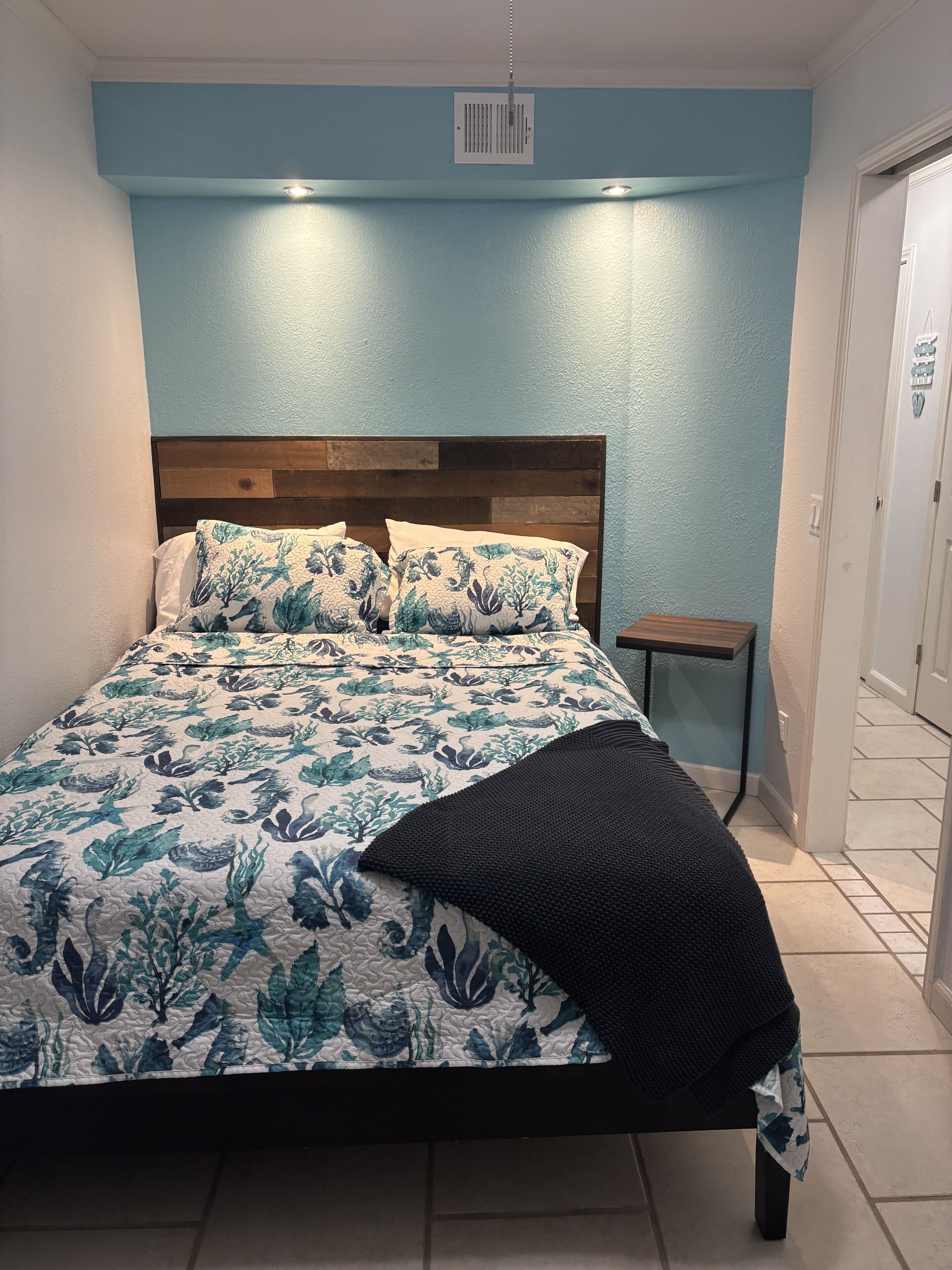 Un lit avec une couvre-lit à motifs floraux, une tête de lit en bois et une petite table de chevet avec une lampe.