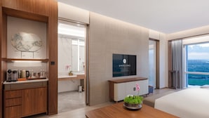 A modern hotel room with a wooden desk, a flat-screen TV, a bed, and a large window with a city view. - Suzhou International Conference Hotel (Suzhou)