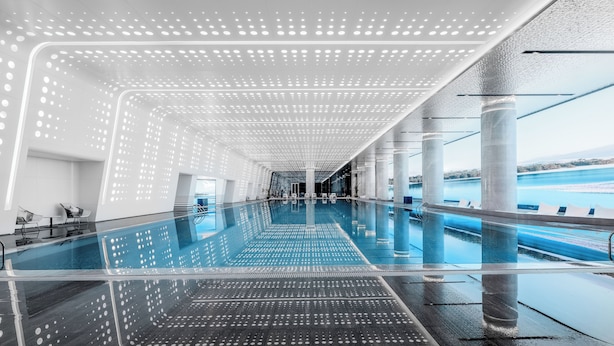 A modern indoor swimming pool with a reflective floor and ceiling, surrounded by columns and a view of a body of water. - Suzhou International Conference Hotel (Suzhou)