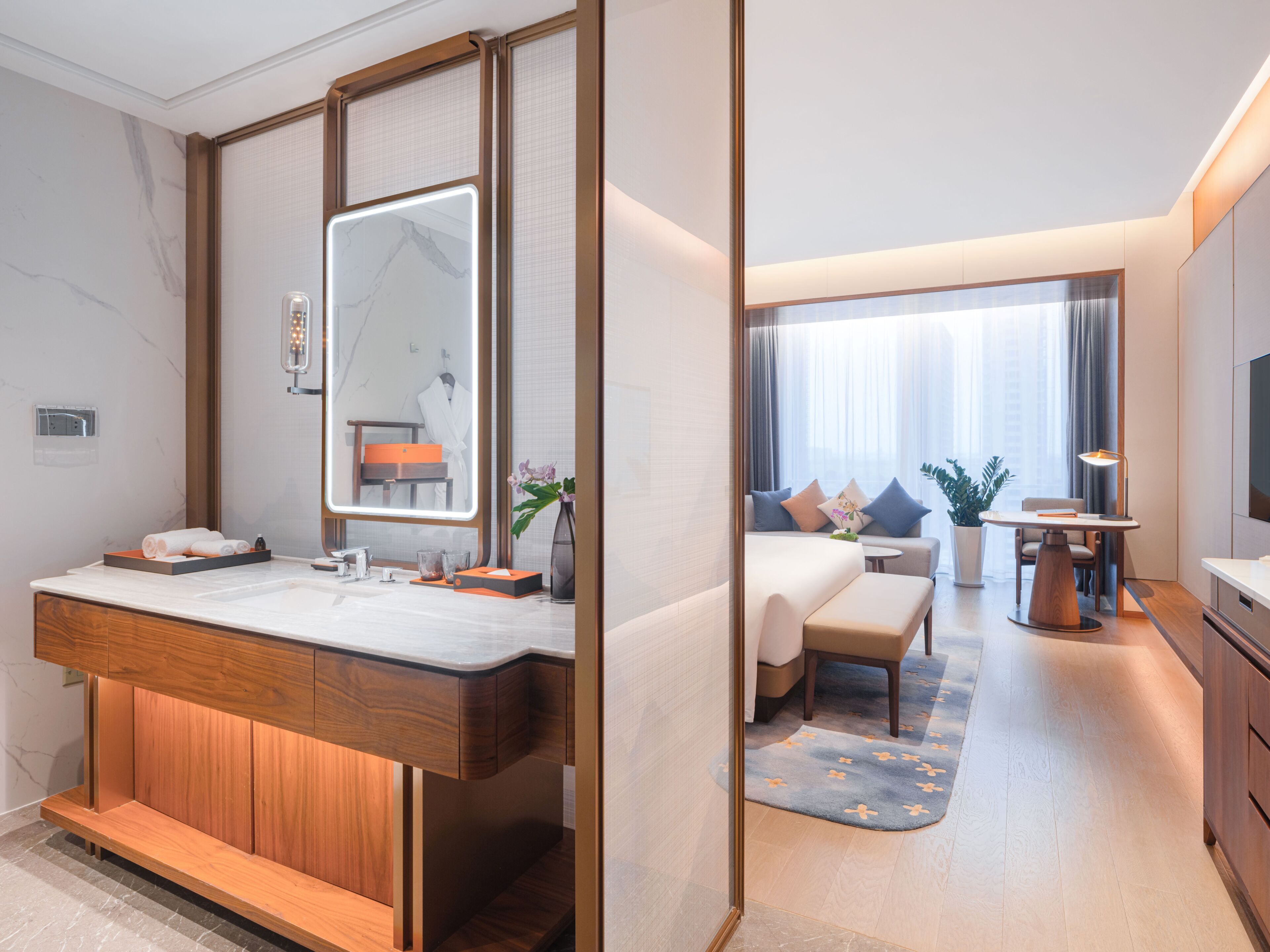 Una habitación de hotel moderna con un tocador de madera, un espejo grande, una cama con vistas, una mesita pequeña y un televisor.