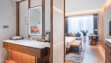 Una habitación de hotel moderna con un tocador de madera, un espejo grande, una cama con vistas, una mesita pequeña y un televisor.