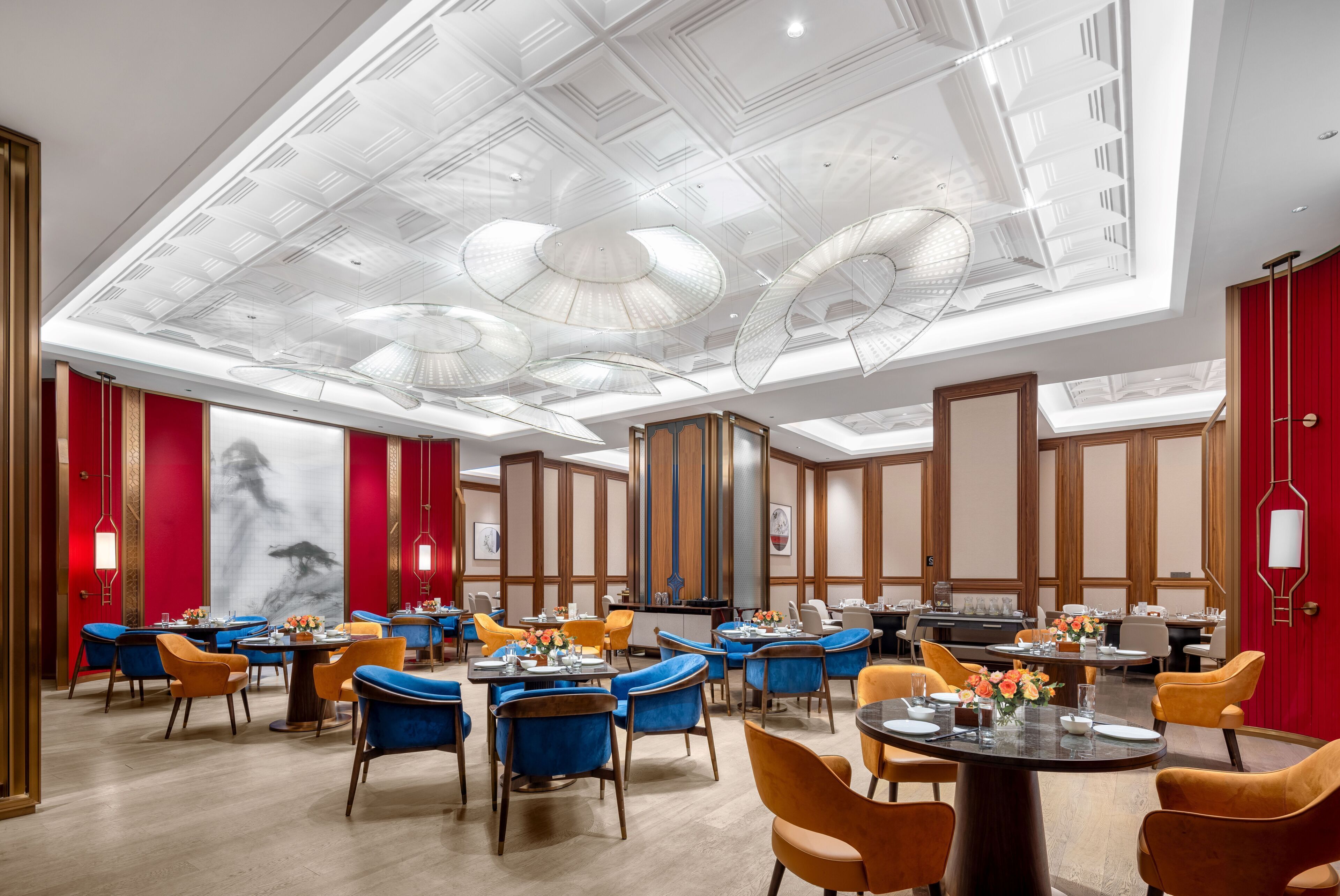 A spacious hotel dining area with multiple tables and chairs, a high ceiling with intricate designs, and a large mural on the wall.
