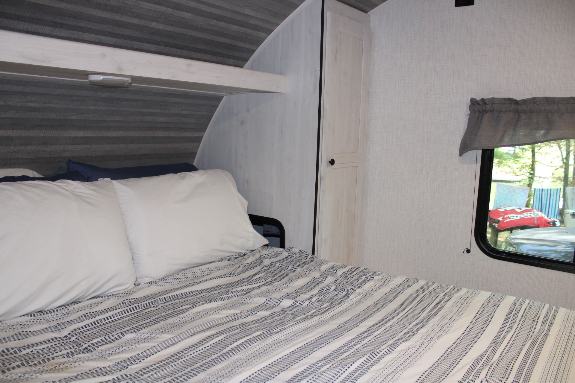 A compact RV interior with a bed, a window, and a door.