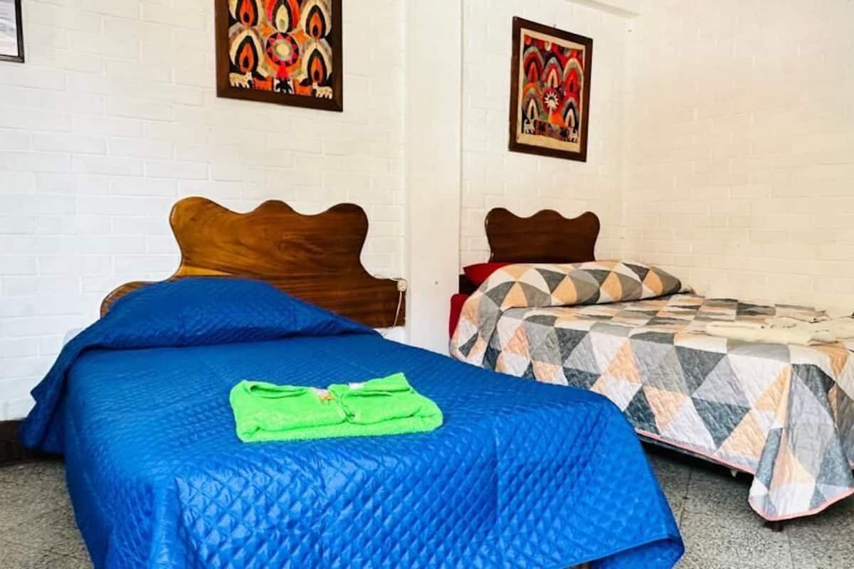 A room with two beds, each with a distinct headboard design. The beds are covered with different patterned bedspreads.