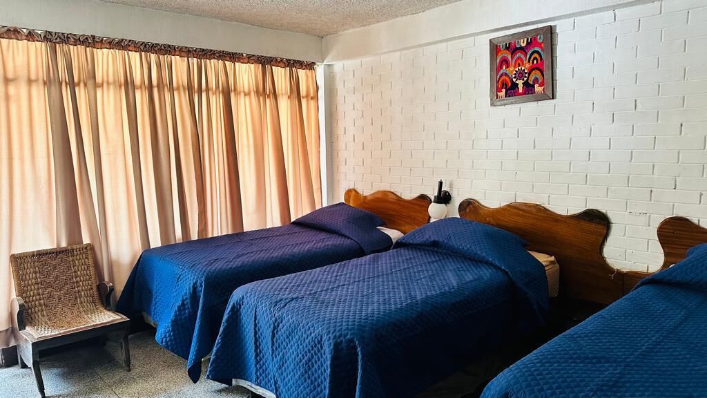 A hotel room with two beds, a chair, and a white brick wall.
