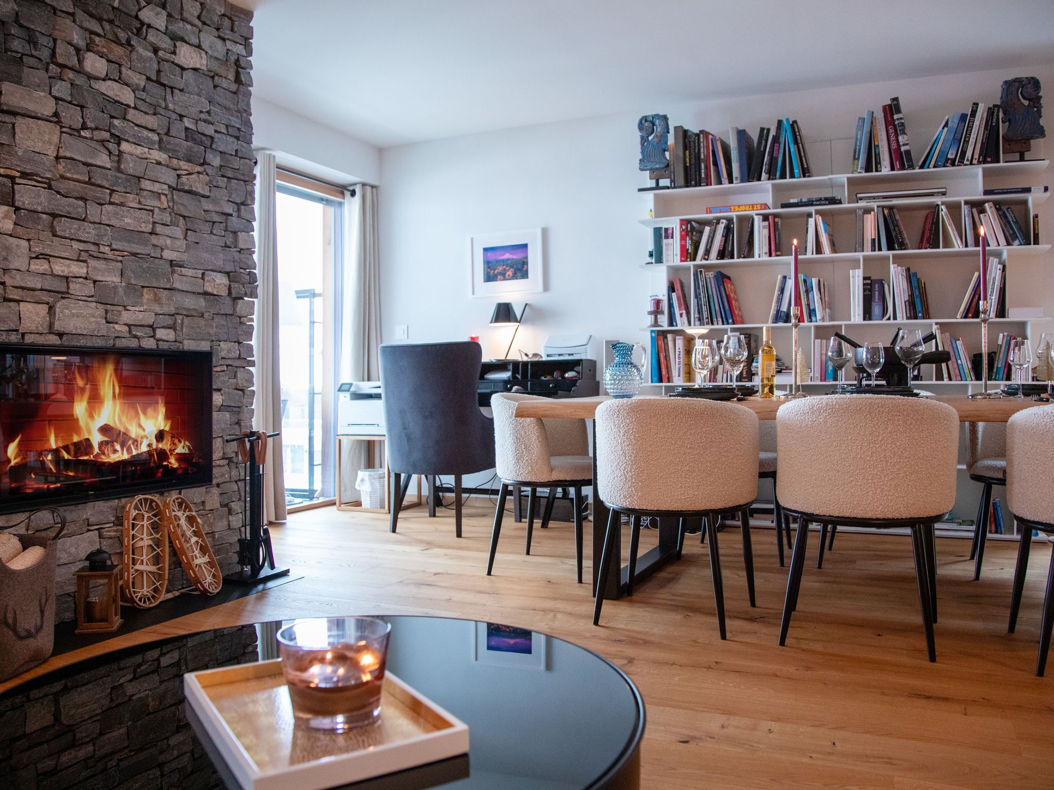 A modern living room with a stone fireplace, a bookshelf, and a dining area with chairs.