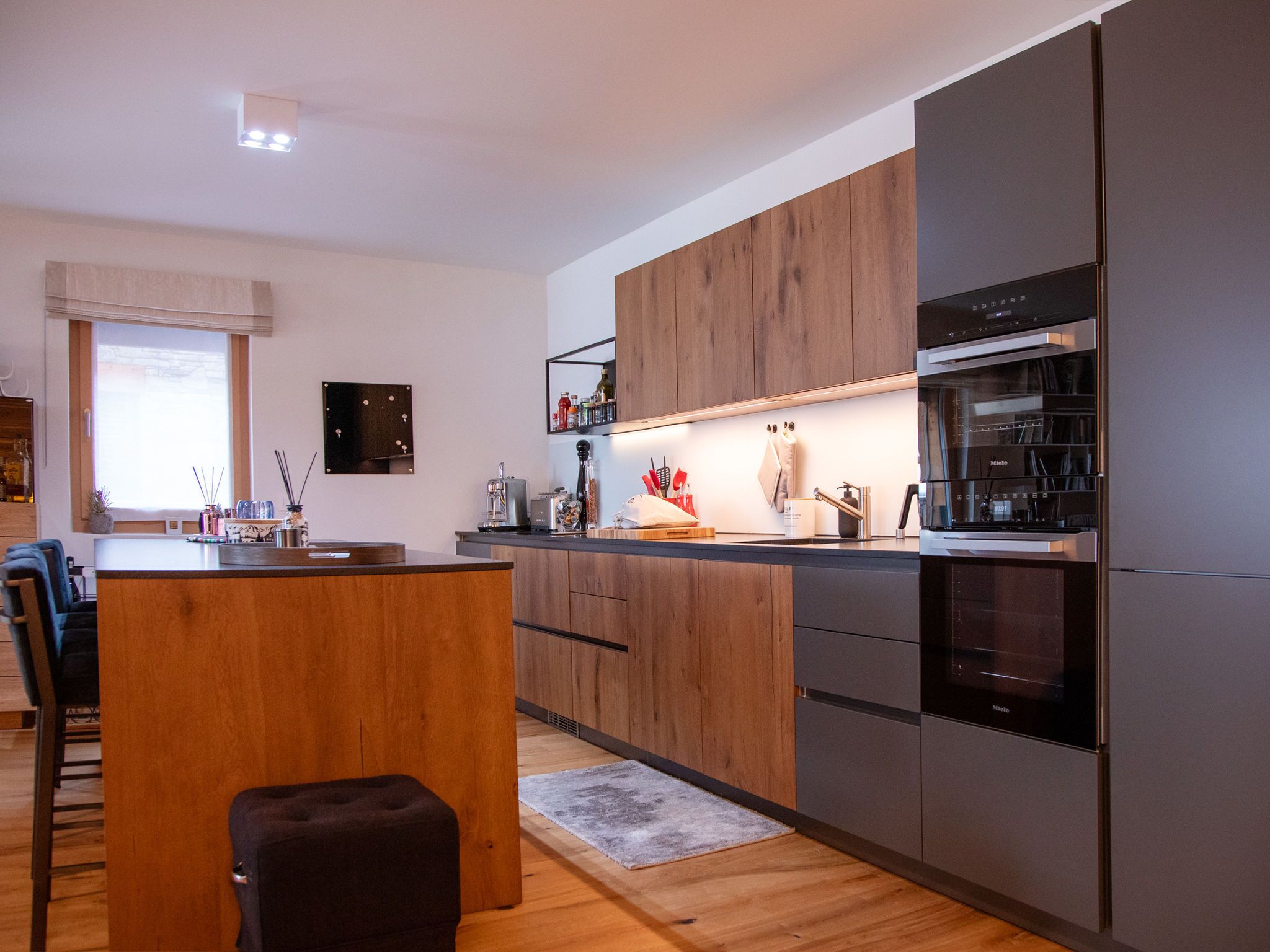 A modern kitchen with wooden cabinets, a built-in oven, and a dining area with a wooden table and chairs.