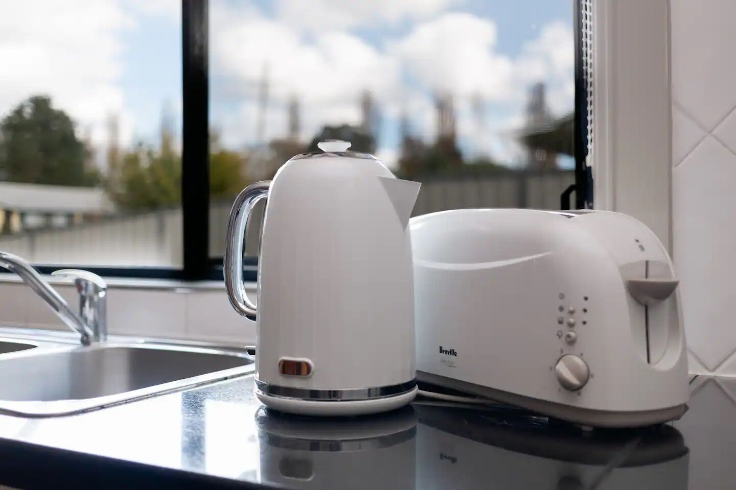 Une machine à café et un grille-pain de la marque Breville sont posés sur un plan de travail de cuisine, près d’une fenêtre.
