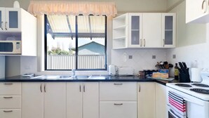 Una cucina con mobili bianchi, un piano di lavoro nero, una finestra con tenda leggera, un fornello e un tostapane.