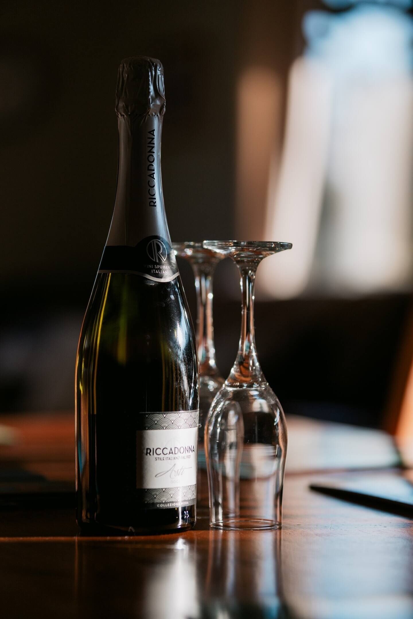 Una botella de vino RICCADONNA con dos copas de vino vacías sobre una mesa de madera.