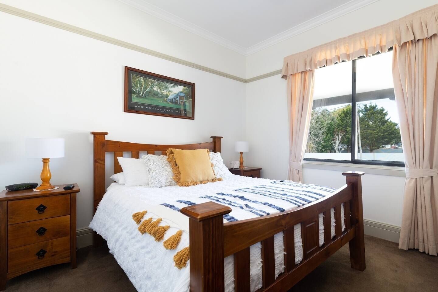 A neatly arranged bedroom with a wooden bed, white bedding, and a window with curtains.