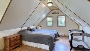 Un dormitorio con techo inclinado, una cama, un aparador de madera y un cochecito de bebé.