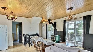 Una sala de estar acogedora con chimenea, piso de madera, un sofá, una mesa de comedor con sillas y vistas al exterior.