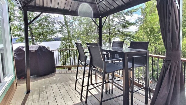 Una terraza techada al aire libre con una mesa y sillas, con vistas a un cuerpo de agua.