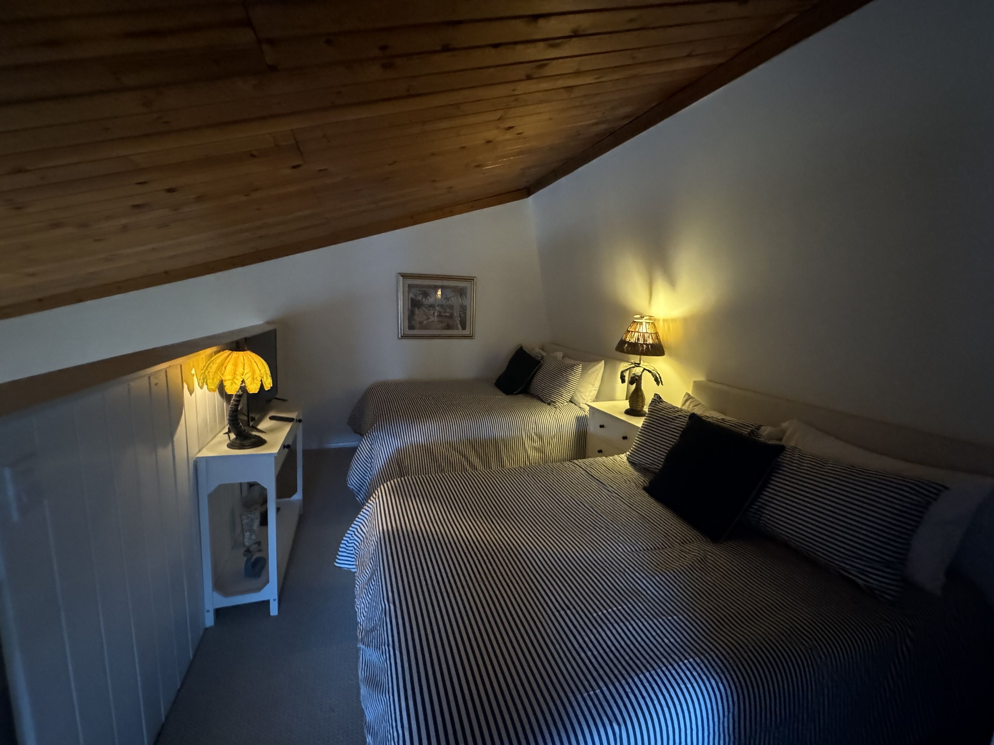 Um quarto de sótão acolhedor com duas camas, uma mesinha e uma luminária.