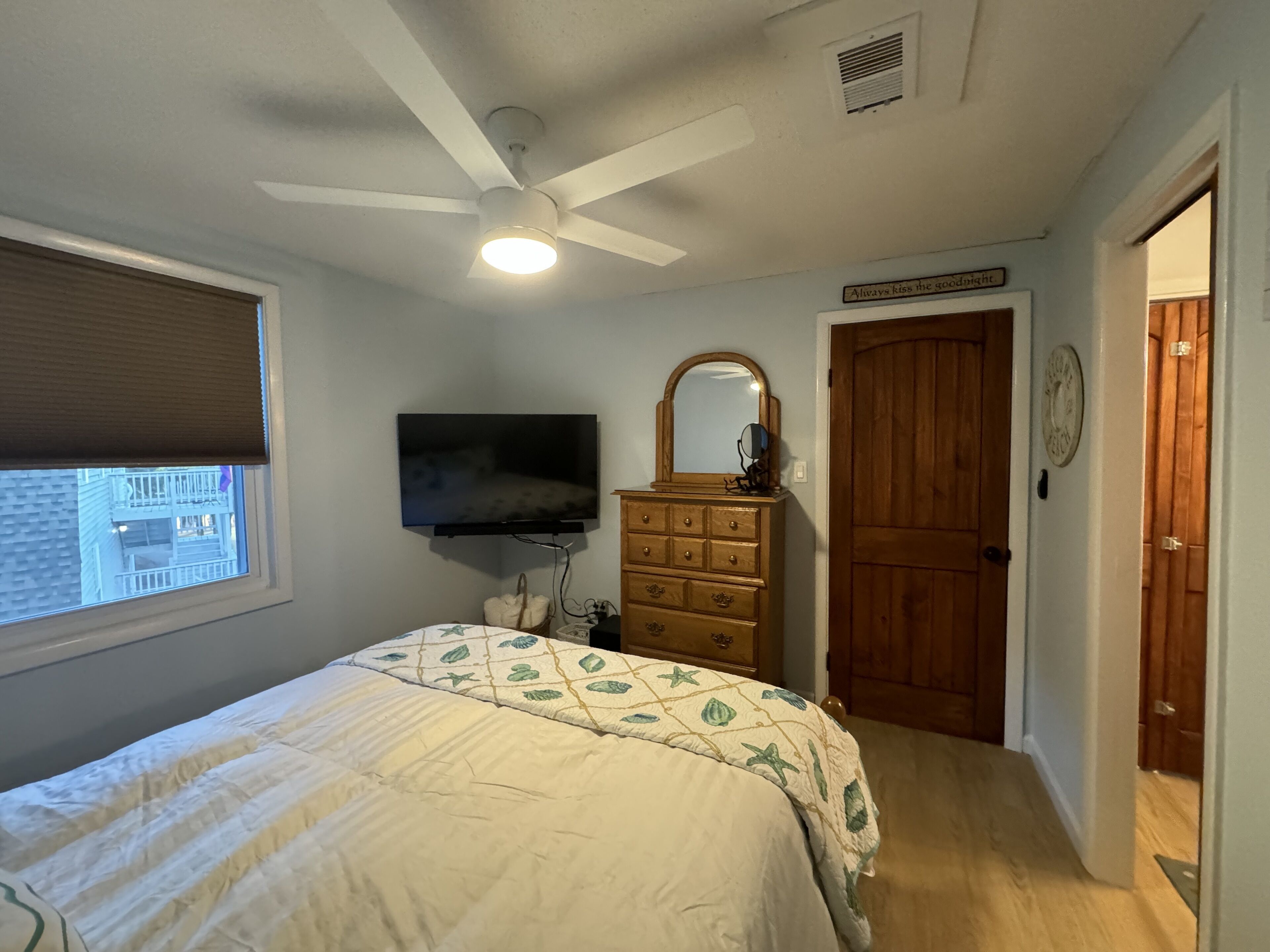 A bedroom with a bed, a dresser, a mirror, a ceiling fan, and a window with blinds.