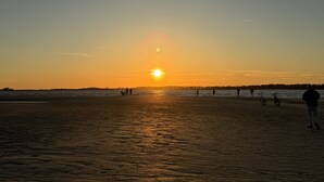Uma praia ao pôr do sol com pessoas caminhando e bicicletas estacionadas.