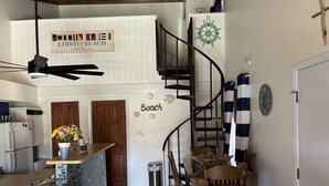 Uma cozinha com ilha de madeira, uma sala de jantar com mesa e cadeiras de madeira, uma escada em espiral e uma placa com a inscrição 'Edisto Beach'.