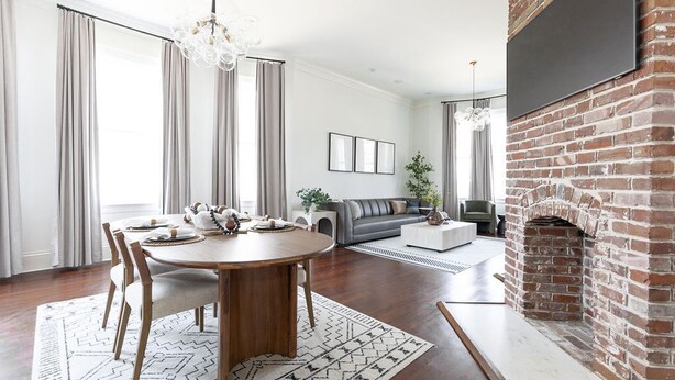 A modern living room with a dining area, a fireplace, and a large TV mounted on a brick wall. - Historic Charleston meets Modern luxury  (Charleston)